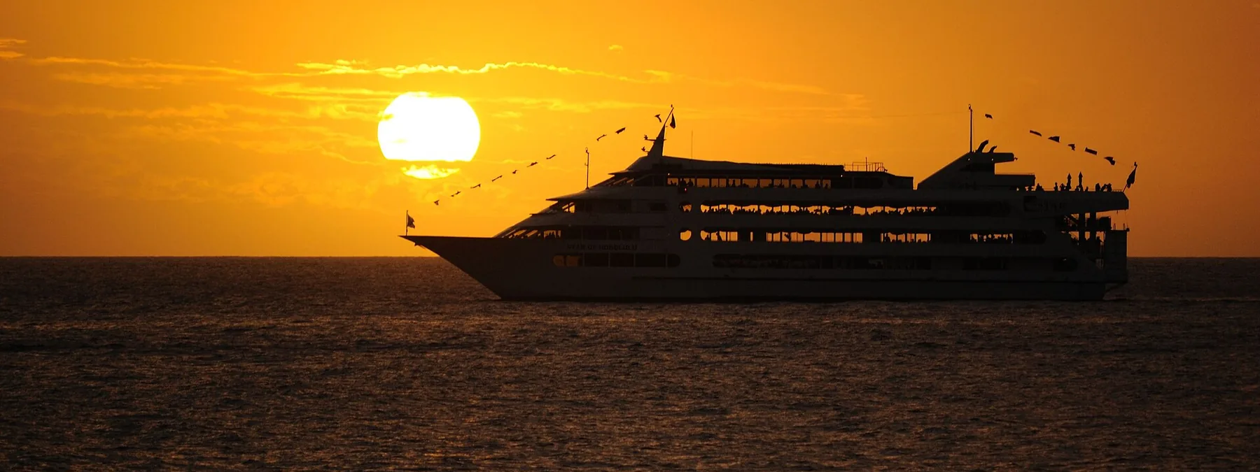 Die Star of Honolulu als dunkle Silhouette vor einem orangefarbenen Sonnenuntergang mit der tief über dem Meer stehenden Sonne